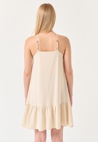 Beiges ärmelloses Kleid aus weichem Stoff mit verstellbaren Trägern, entspannter Passform und Rüschensaum.