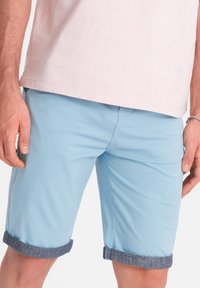 Světlé modré bavlněné šortky s ohrnutým lemem v denimu, texturovaná tkanina, boční kapsy a volný střih, doplněné o světle růžové tričko.