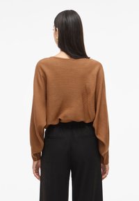 Pull en tricot côtelé marron avec une coupe décontractée et des manches larges, associé à un pantalon noir taille haute. Texture lisse et design décontracté.
