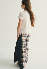 Krémové tričko s krátkym rukávom skombinované s károvanými nohavicami v krémovej, námorníckej a červenej farbe. Drží tmavomodrý pletený menjal. Jednoduchý a voľný strih.