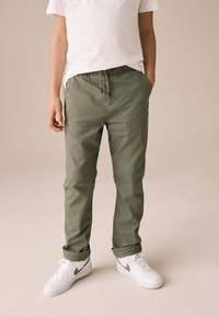Spodnie w kolorze oliwkowej zieleni wykonane z bawełny o luźnym kroju, z elastycznym pasem i sznurkiem, zestawione z białymi trampkami.