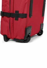 Valigia da viaggio rossa realizzata in tessuto resistente, con angoli in plastica nera e quattro ruote girevoli per stabilità e facile mobilità.