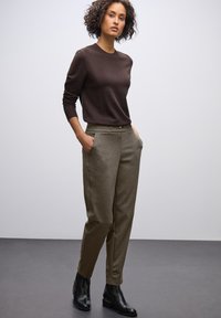 Brun tröja med långa ärmar, kombinerad med löst sittande olivgröna byxor. Svarta ankelstövlar med en liten klack fulländar outfiten.