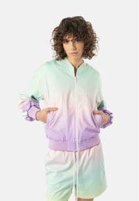 Lett boblejakke med gradient fra mint til lavendel. Har glidelås foran, ribbestrikkede mansjetter og sidelommer. Kombinert med matchende shorts.