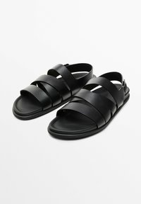 Black leather sandals featuring multiple wide straps and an open back design with a buckle closure. Flat sole, smooth texture.