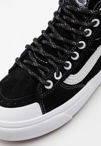 Černé semišové tenisky s bílou gumovou podrážkou, které mají černobílé tkaničky, kontrastní švy a výrazné boční logo.