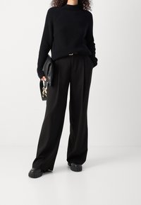Maglione a coste nero con collo alto, abbinato a pantaloni neri larghi. Gli accessori comprendono una pochette nera e scarpe con piattaforma chunky.