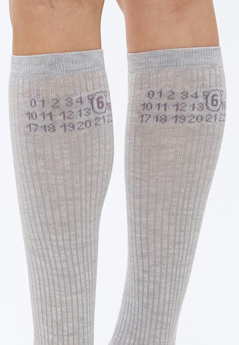 Grå knæstrømper med lodret ribstruktur. Har trykt taldesign på siden og en cirkulær logo nær den øverste kant.