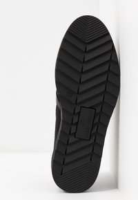 Semelle de chaussure en caoutchouc noir avec un motif de bande de roulement en chevrons prononcé, marquée "ANNA FIELD" et taille 37, avec des bords texturés pour une meilleure adhérence.