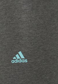 Grå sporttröja av mjukt, strukturerat tyg med en turkos Adidas-logotyp i nedre vänstra hörnet.