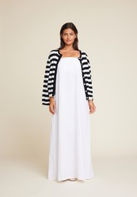 Hvit, ermeløs maxikjole med rett utringning, lagd med en svart og hvit stripete cardigan med knapper og trekvartlange ermer.