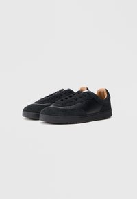 Zapatillas negras hechas de ante y cuero texturizado, con una suela negra lisa y un forro interior en color marrón claro. Diseño con cordones y perforaciones.