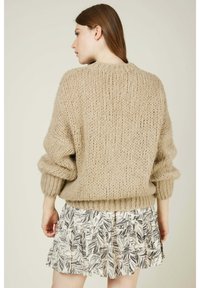 Pull en tricot beige chunky avec un col rond et des épaules tombantes, assorti à une jupe blanche à motifs avec des imprimés de feuilles.