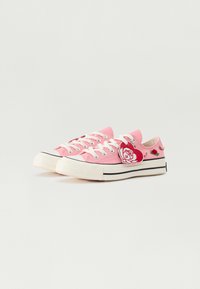 Zapatillas de lona rosas con cordones blancos, suela de goma negra y adornos de rosa. Presentan puntera redonda y detalles de franjas laterales en contraste.