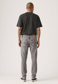 Γκρι τζιν από τζιν ύφασμα με ίσια γραμμή, με πίσω τσέπες και καφέ δερμάτινο ταμπελάκι στη μέση. Συνδυασμένο με μαύρη μπλούζα και αθλητικά παπούτσια.