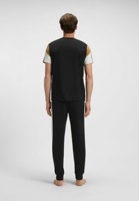 Czarny zestaw piżamowy składający się z koszulki z krótkim rękawem z złotymi i białymi akcentami oraz pasujących czarnych spodni, obie części o gładkiej fakturze.