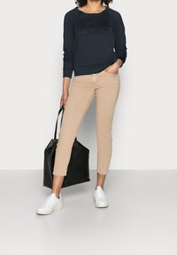 Námořnická mikina s embossovaným logem, béžové cropped kalhoty, černá taška a bílé tenisky. Měkká tkanina, volný střih a minimalistický design.