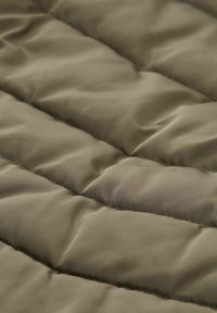 Zbliżenie na oliwkowy, pikowany materiał z poziomymi szwami i miękką, wyściełaną teksturą.