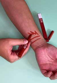 Red marker pen applied to the forearm, leaving three bold strokes. The pen features a cylindrical shape with a cap and a flat design.