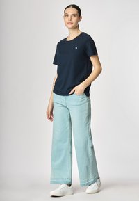 T-shirt navy a maniche corte con un piccolo accento ricamato, abbinato a jeans a gamba larga blu chiaro e sneakers bianche.