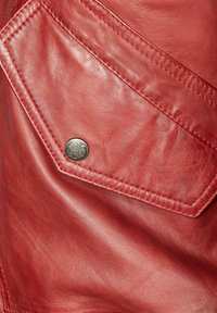 Rotes Ledergewebe mit einer diagonalen Tasche und einem silbernen Knopf. Glatte Textur mit sichtbaren Nähten.