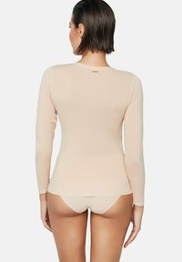 Top nude à manches longues avec une texture lisse et extensible, présentant un logo subtil au niveau du col et un design ajusté.