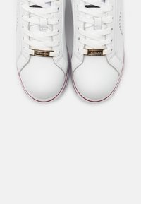 Paire de baskets en cuir blanc avec des lacets blancs et des étiquettes dorées "Trussardi" sur les languettes, sur un fond uni.