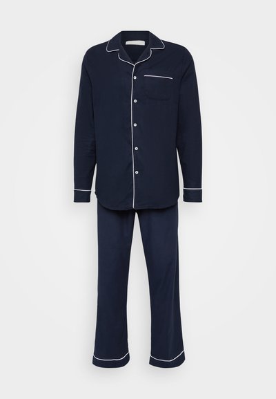 Tumši zila kokvilnas pidžamu komplekts, kas ietver apkakles garām piedurknēm topu ar baltu apdari un atbilstošus bikses ar taisnu piegriezumu un apdari pie galiem.