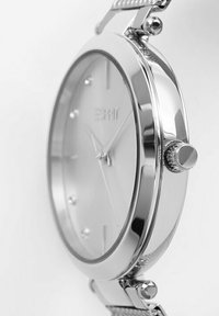 Orologio in metallo argento con cassa rotonda, quadrante liscio e indicatori delle ore minimalisti. Presenta un cinturino testurizzato e una corona prominente.