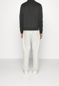 Sudadera negra con cuello alto, combinada con pantalones a rayas blancos y gris claro. Presenta un corte holgado y zapatillas blancas.