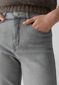 Jeans in denim grigio con vita alta, dotati di una tasca frontale, dettagli cuciti e una chiusura con bottone metallico in vita.