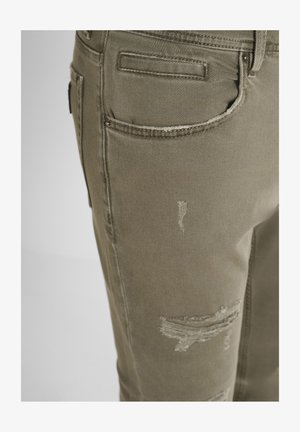 Close-up van een paar khaki versleten jeans met details van de voorkzak en rafelige stofgebieden op de dij.