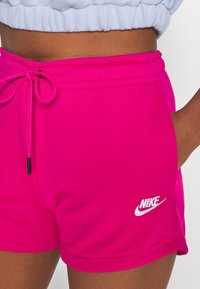 Růžové šortky Nike s šňůrkou v pase, bočními kapsami a logem v bílé barvě. Vyrobeny z hladkého materiálu s těsným střihem.