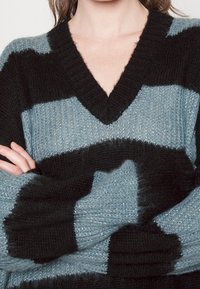 Black and light blue striped sweater with a V-neck, knitted texture, and a slight shimmer. Loose fit with wide sleeves and cuffs.
