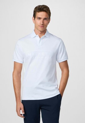 Camisa polo blanca con un sutil logo "HACKETT", mangas cortas y un cuello clásico. El material parece suave y ligero.