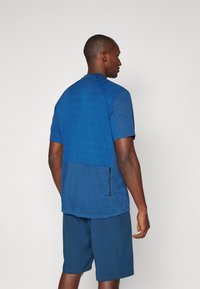 Camisa atlética de manga curta e calções em diferentes tons de azul. A camisa apresenta um design texturizado com um detalhe de fecho de lado.