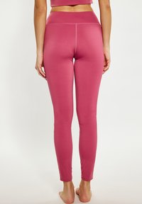 Strakke roze leggings van een gladde stof, met een hoge tailleband en zonder zichtbare patronen of versieringen.