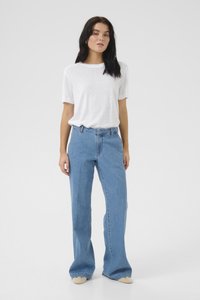 Hvid kortærmet t-shirt parret med lys blå flare jeans, der har høj talje og diskret syninger. Skoene er lyse i farven.