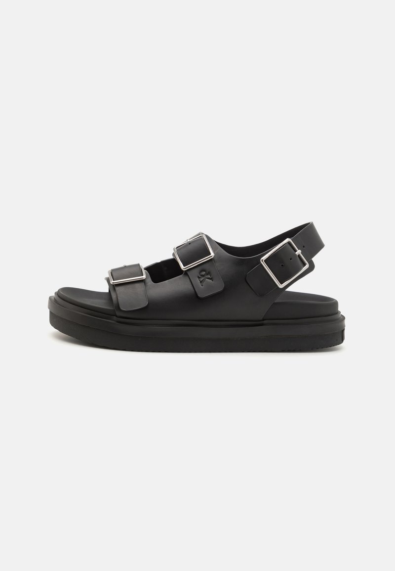 Svarta sandaler med platt sula, utrustade med två justerbara spännen och ett bakre rem. Tillverkade av slätt syntetmaterial med en ren design.