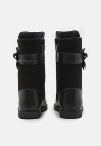 Mustat saapasmainen kengät, joissa on mokkanahka- ja nahkamateriaalit, sileä pinta, pyöreä kärki ja solk yksityiskohtia sivuilla.