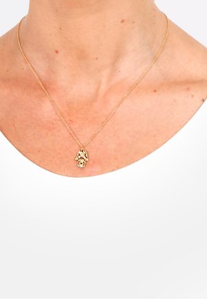 Collier en chaîne d'or avec un pendentif détaillé de main de Hamsa porté autour du cou d'une personne au-dessus d'un haut blanc.