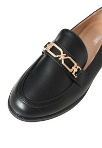 Mocassino in pelle nera con punta arrotondata, caratterizzato da un accento di catena dorata sulla tomaia e dettagli di cucitura delicati. Texture liscia su tutta la scarpa.