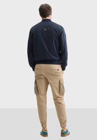 Námořnická bomber bunda, béžové cargo kalhoty se stahovacími manžetami a vícebarevné tenisky. Výrazné kapsy na kalhotách, strukturovaná látka na bundě.