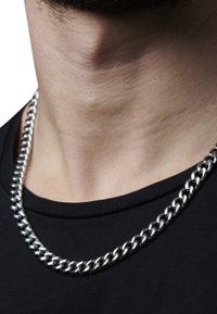 Silberne Metallkette mit einem dicken, ineinandergreifenden Glieddesign. Über einem schwarzen Hemd getragen, hebt sie die glänzende Textur und das Muster hervor.