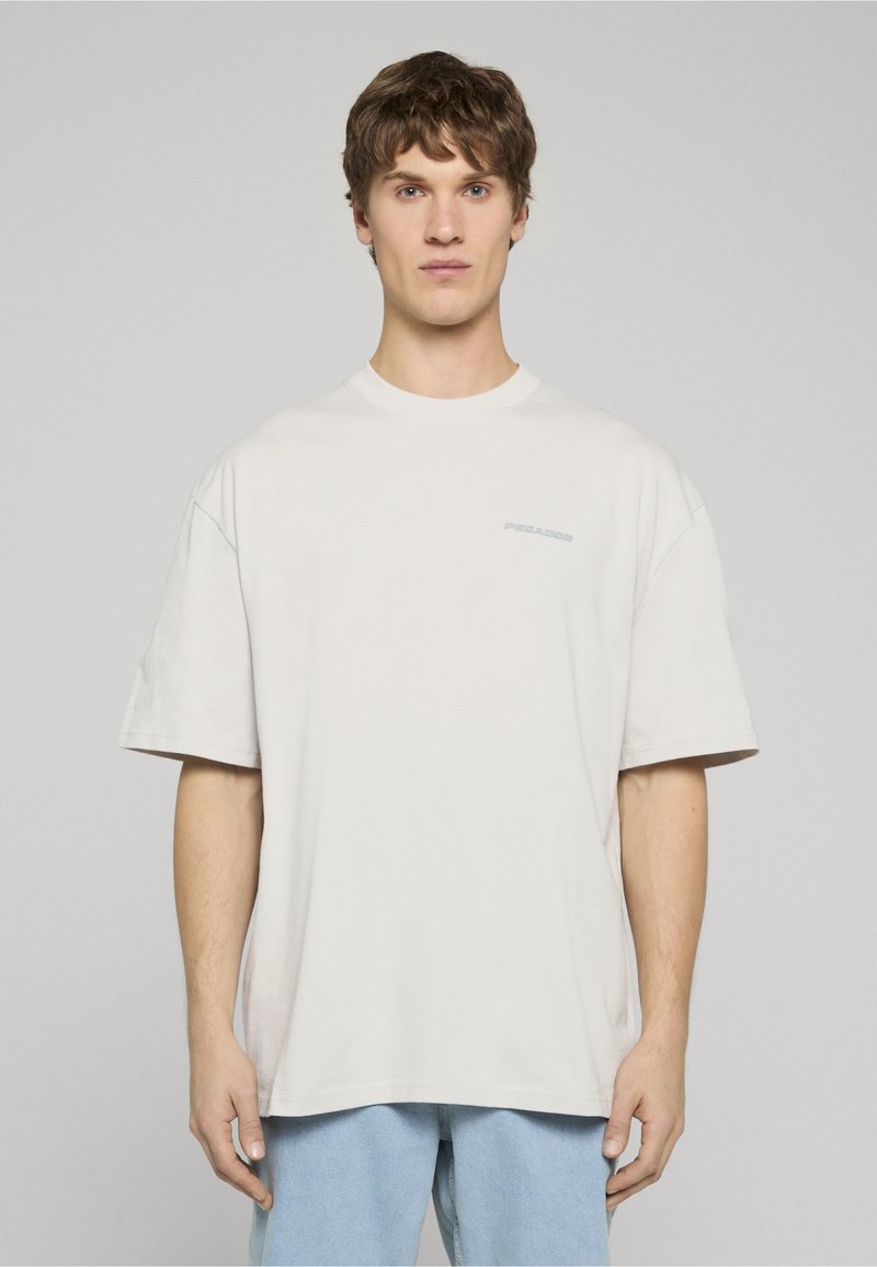 Světlé béžové oversized bavlněné tričko s kulatým výstřihem a krátkými rukávy. Na hrudi má jemné logo. Jednoduchý design.