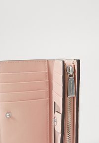 Portafoglio rosa chiaro con molteplici fessure per schede, un compartimento con zip e hardware in tono argento. Texture liscia con bordi scuri a contrasto.