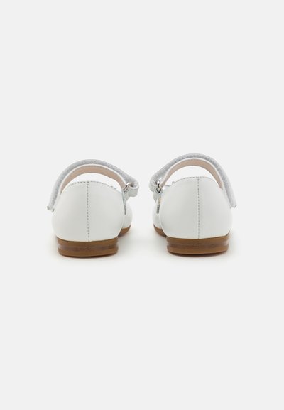 Zapatos de cuero blancos con punta redondeada, suela plana marrón y correas ajustables grises en la parte trasera para un ajuste seguro. Diseño simple y líneas limpias.