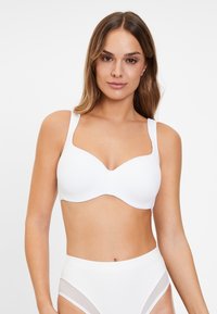 Witte bh met gladde cups en brede bandjes. Beschikt over een subtiele V-halslijn en een naadloos ontwerp, gecombineerd met hoge witte slips.