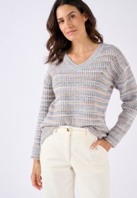 V-hals trui van een lichte, gestructureerde brei met pastelstrepen in blauw en beige, gedragen over crèmekleurige corduroybroek.