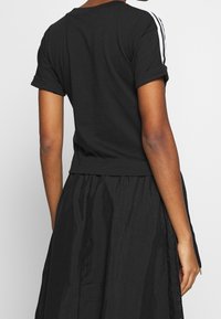 T-shirt nero a maniche corte con bordo arrotolato e strisce bianche sulle spalle, realizzato in un morbido cotone.